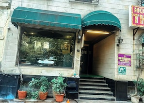 A building with a large window, a green awning, and a sign indicating an assembly station. - The Metropolis Guest House Near RK Ashram Metro Station (New Delhi)
