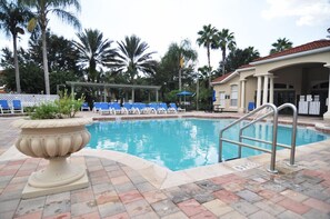 Une piscine avec des chaises longues, une pergola, des palmiers et un bâtiment doté d’un toit en tuiles.