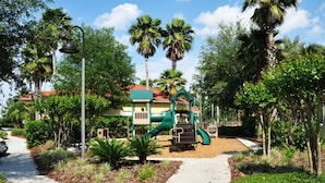 Ein Spielplatz mit Rutsche und Klettergerüst, umgeben von Palmen und einem Weg.