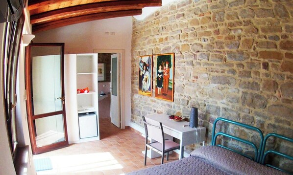 Una habitación con pared de piedra, cama con estructura metálica, escritorio con silla y armario.