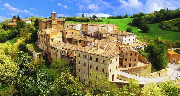 A historic town with a central building surrounded by smaller structures, a clear sky, and lush greenery. - Nidastore B&B (Arcevia)