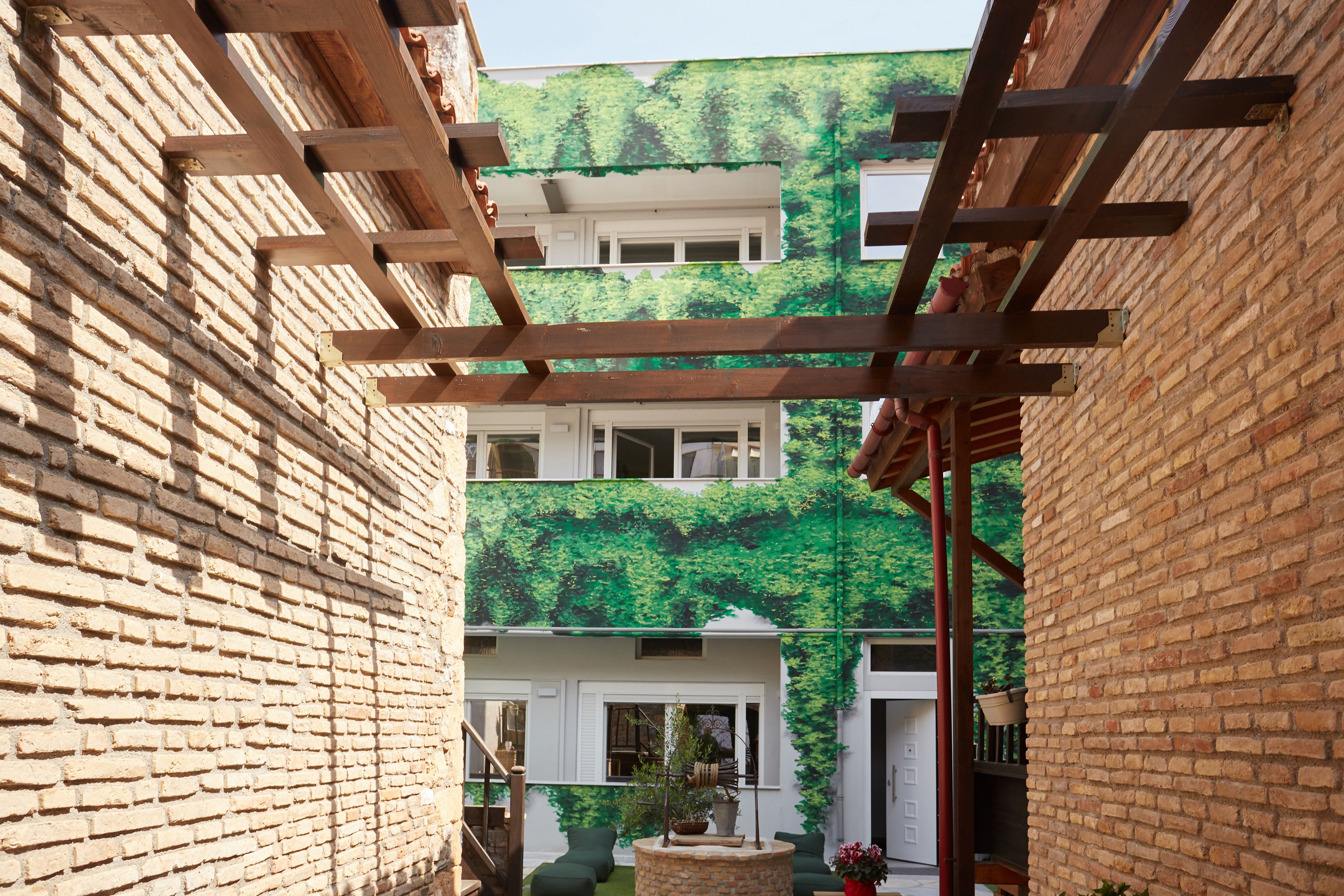 A courtyard with a brick wall, wooden pergola, and a green wall with climbing plants.