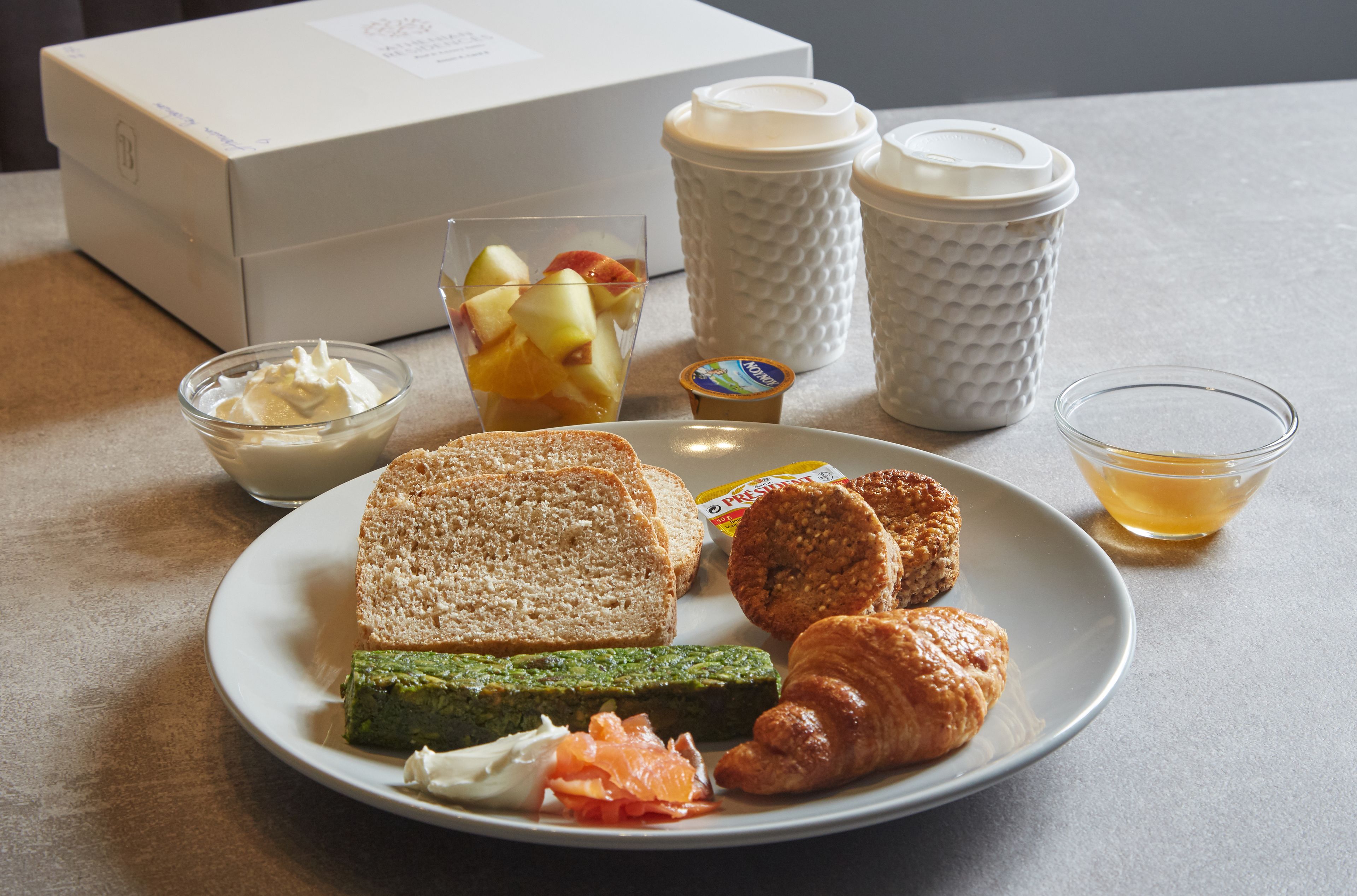 A plate with toast, croissants, and a green spread, a glass of fruit, and a cup of tea on a table.