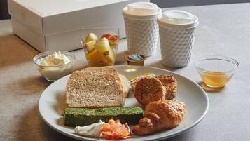 A plate with toast, croissants, and a green spread, a glass of fruit, and a cup of tea on a table.