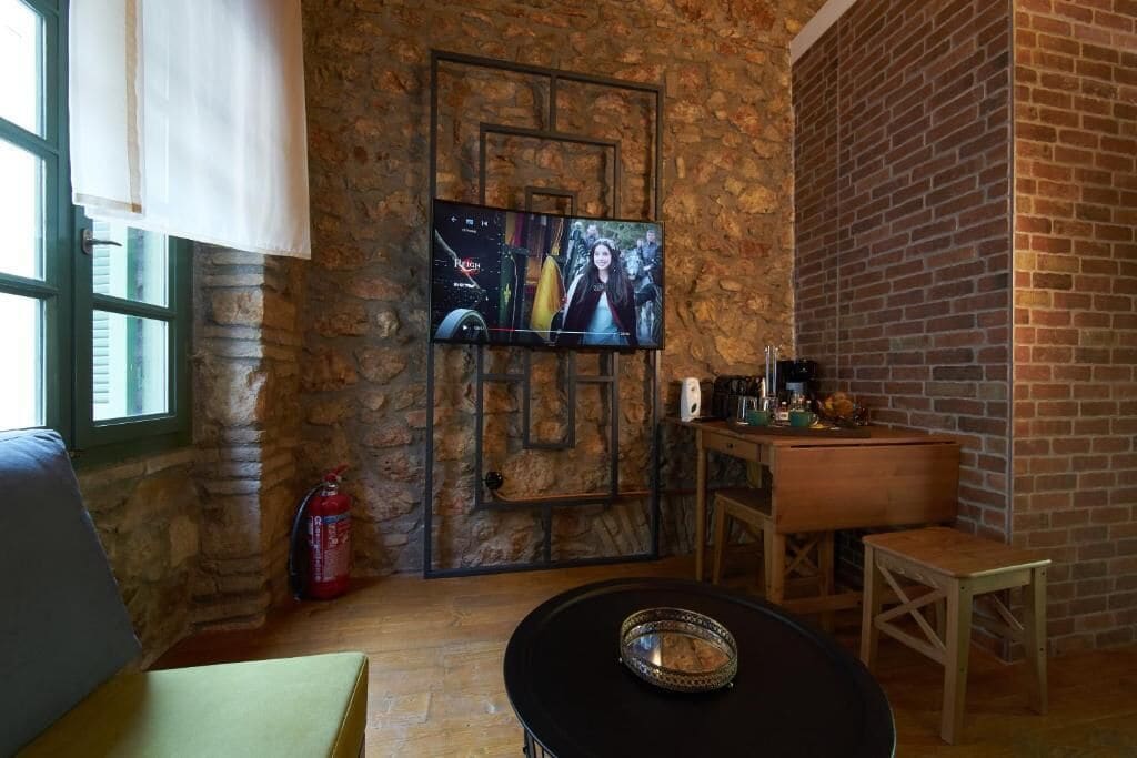 A cozy room with a stone wall, a TV mounted on it, a wooden table, and a fire extinguisher.