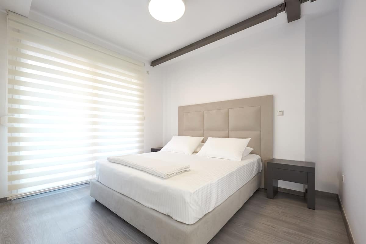 Quarto com cama grande, mesa de cabeceira e janela com persianas.