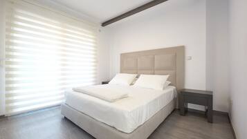 Een slaapkamer met een groot bed, een nachtkastje en een raam met jaloezieën.