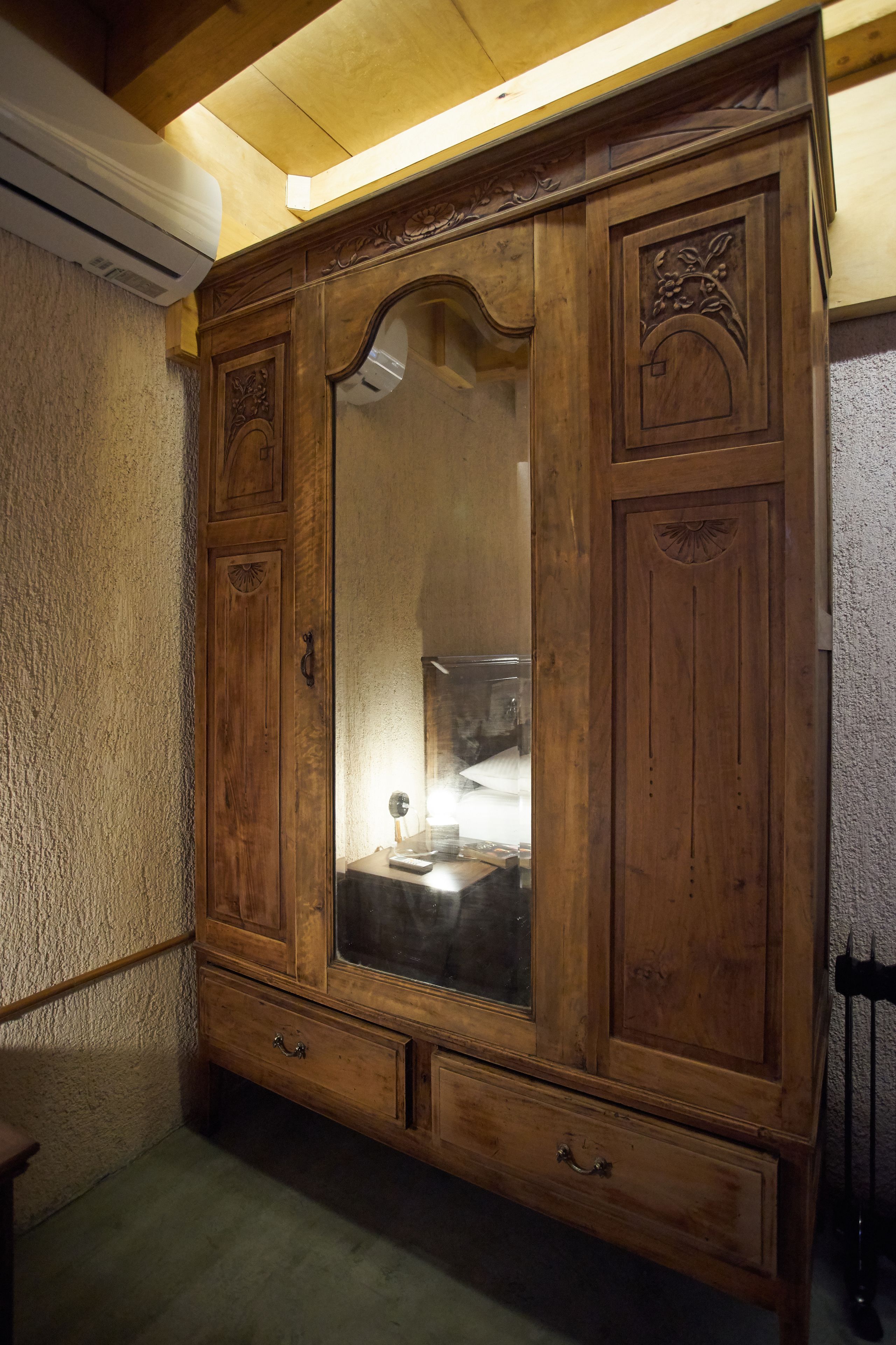 A wooden wardrobe with a mirror, a small table, and a chair.