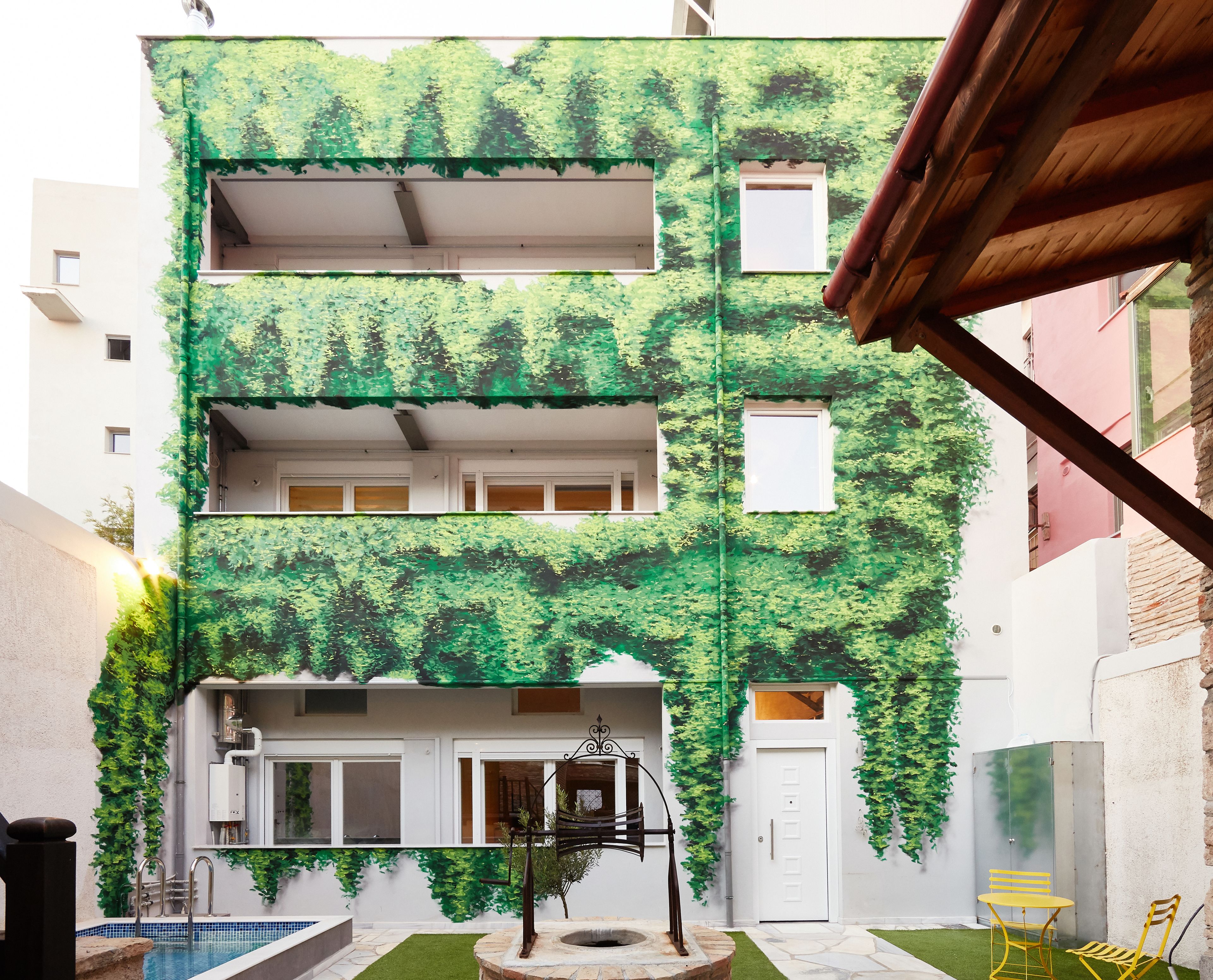 A multi-story building with a green leafy facade, a small pool, and outdoor seating.