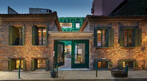 Un bâtiment en pierre avec des volets verts, une porte centrale et un petit jardin.
