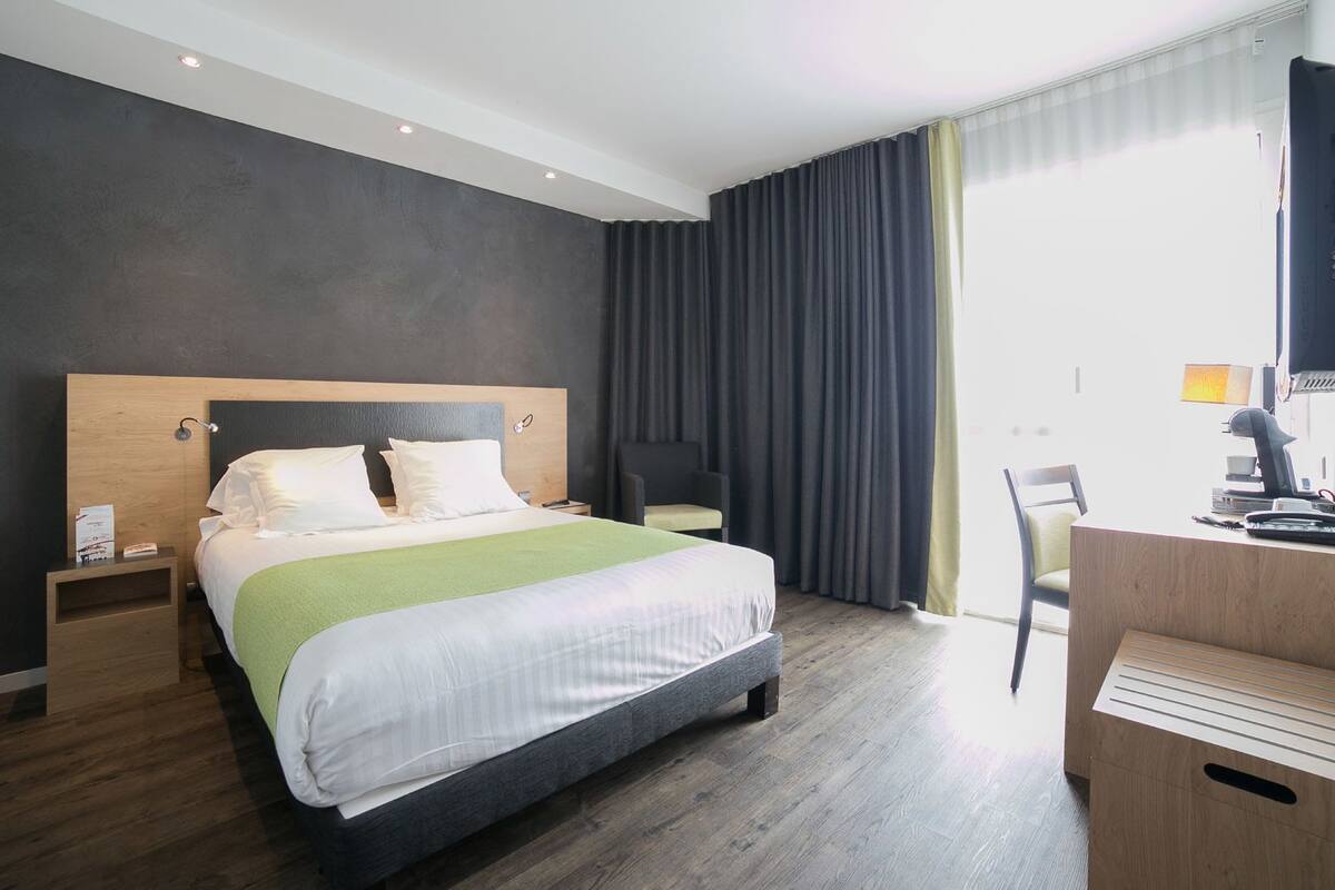 Ett modernt hotellrum med en stor säng, ett skrivbord med en dator och en stol.