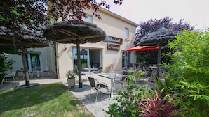 An outdoor seating area with tables and chairs, a thatched umbrella, and a sign for 'Restaurant Le Vigneron'.