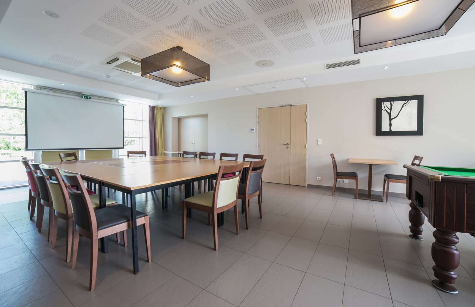 A conference room with a large table, chairs, a projector screen, and a pool table.
