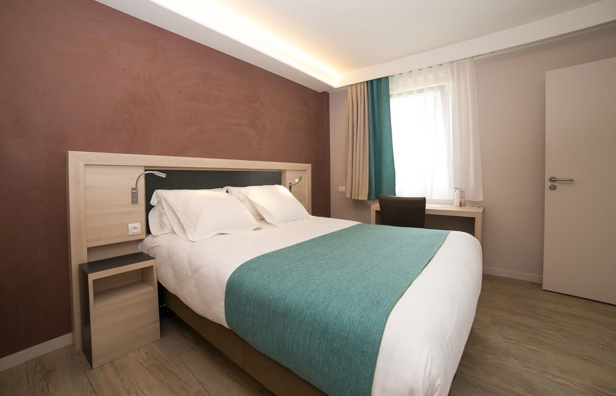 A hotel room with a bed, bedside table, and a desk with a chair.