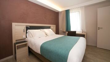 A hotel room with a bed, bedside table, and a desk with a chair.
