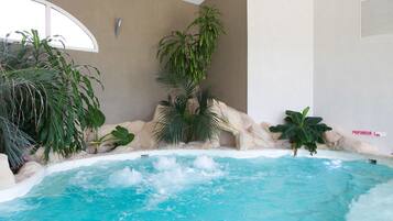 A hot tub with a rocky edge, surrounded by tropical plants and a stone wall.