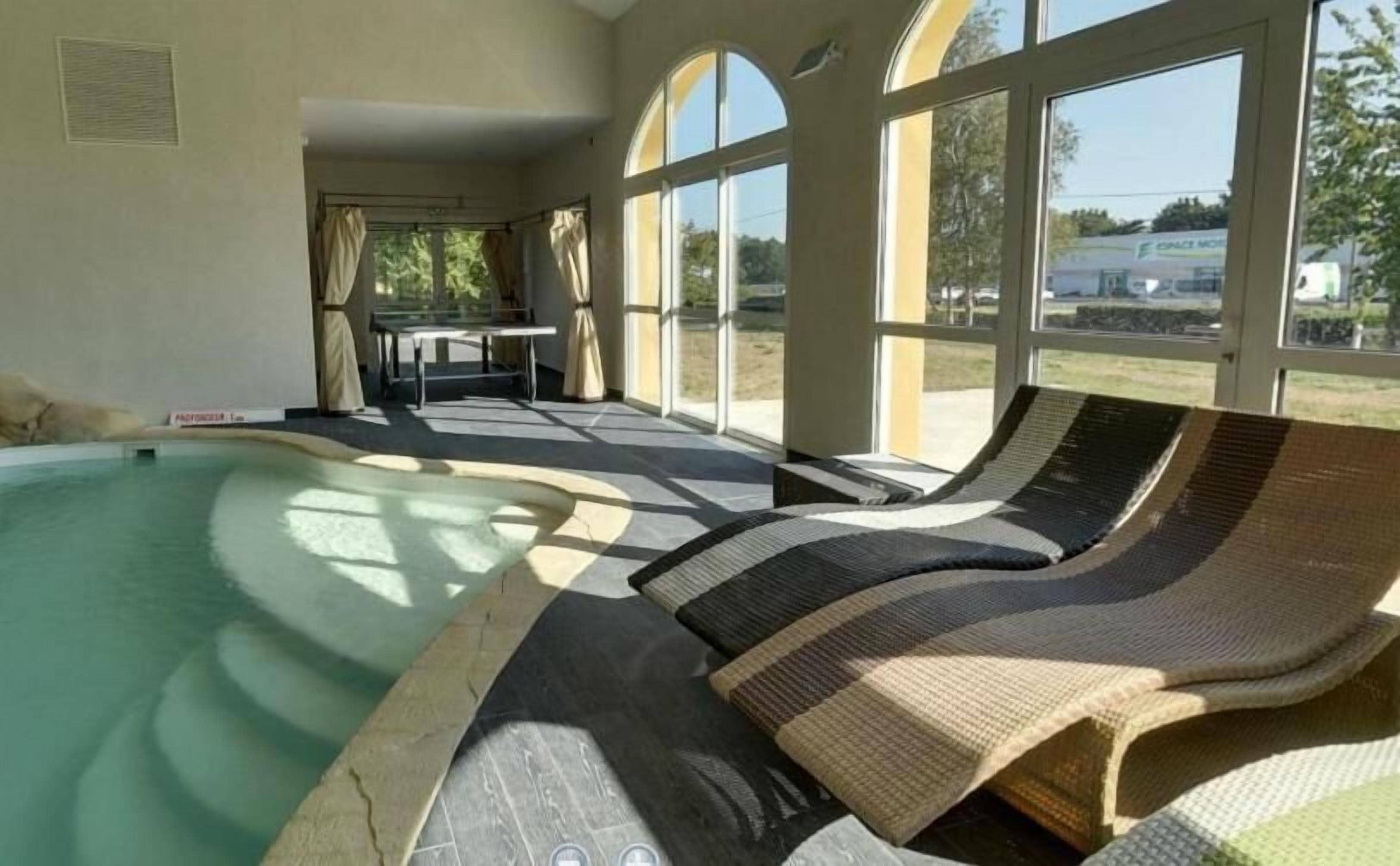 Un espace piscine avec des chaises longues et une table, de grandes fenêtres et une vue sur l’extérieur.