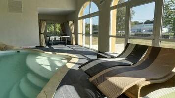 Un espace piscine avec des chaises longues et une table, de grandes fenêtres et une vue sur l’extérieur.
