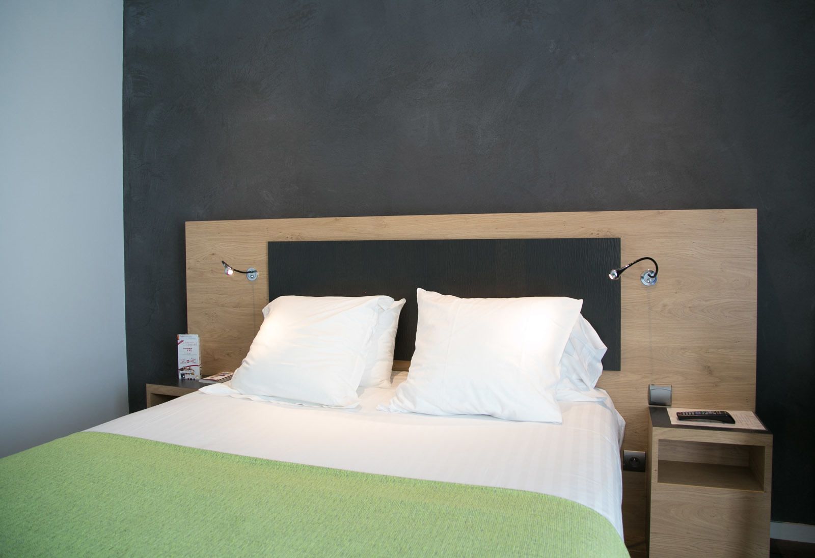 Un letto rifatto con lenzuola bianche, due comodini e una coperta verde.