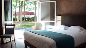 A hotel room with a bed, a chair, and a large window offering a view of trees and a building outside.