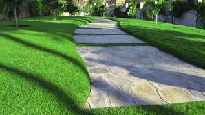 A stone pathway with lush green grass on either side, leading towards a building. - ISAMILO GRAND HOTEL (Mwanza)
