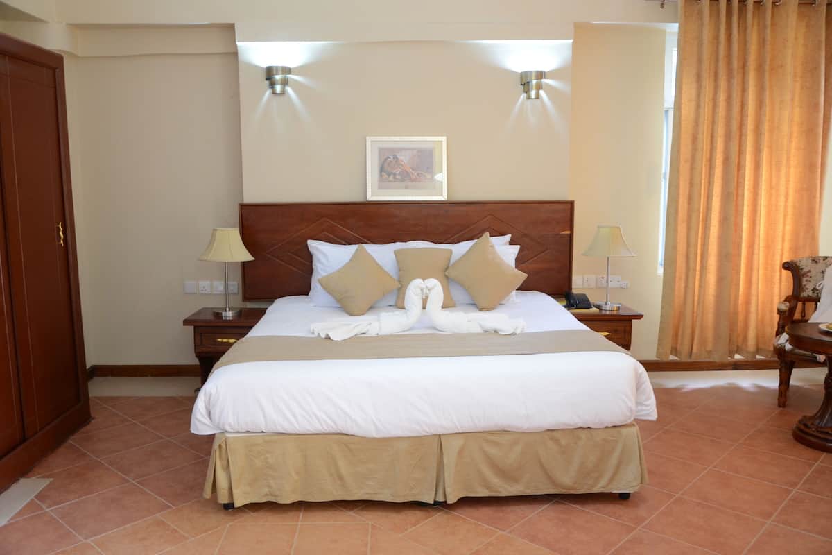 A hotel room with a large bed, two bedside tables, a wooden headboard, a framed picture on the wall, and a curtain on the window.