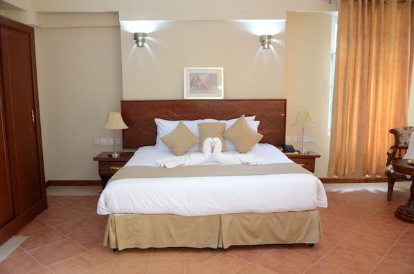 A hotel room with a large bed, two bedside tables, a wooden headboard, a framed picture on the wall, and a curtain on the window. - ISAMILO GRAND HOTEL (Mwanza)