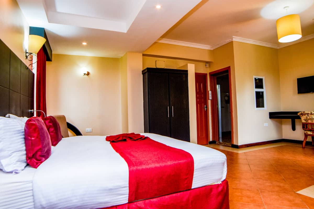 A hotel room with a large bed, a wardrobe, a TV, and a chair.