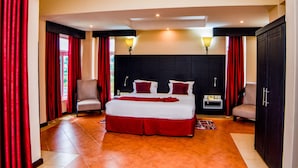 A hotel room with a large bed, two armchairs, a nightstand, and a wardrobe. - ISAMILO GRAND HOTEL (Mwanza)