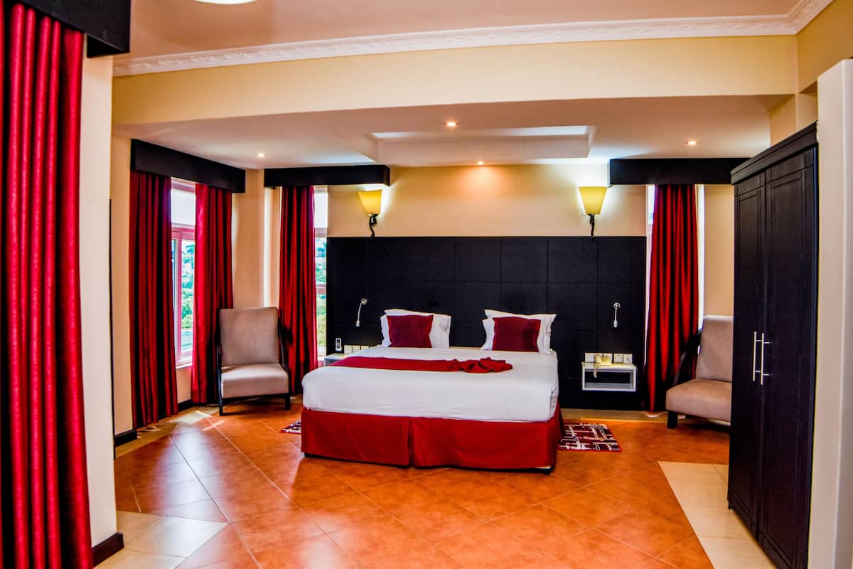 A hotel room with a large bed, two armchairs, a nightstand, and a wardrobe.
