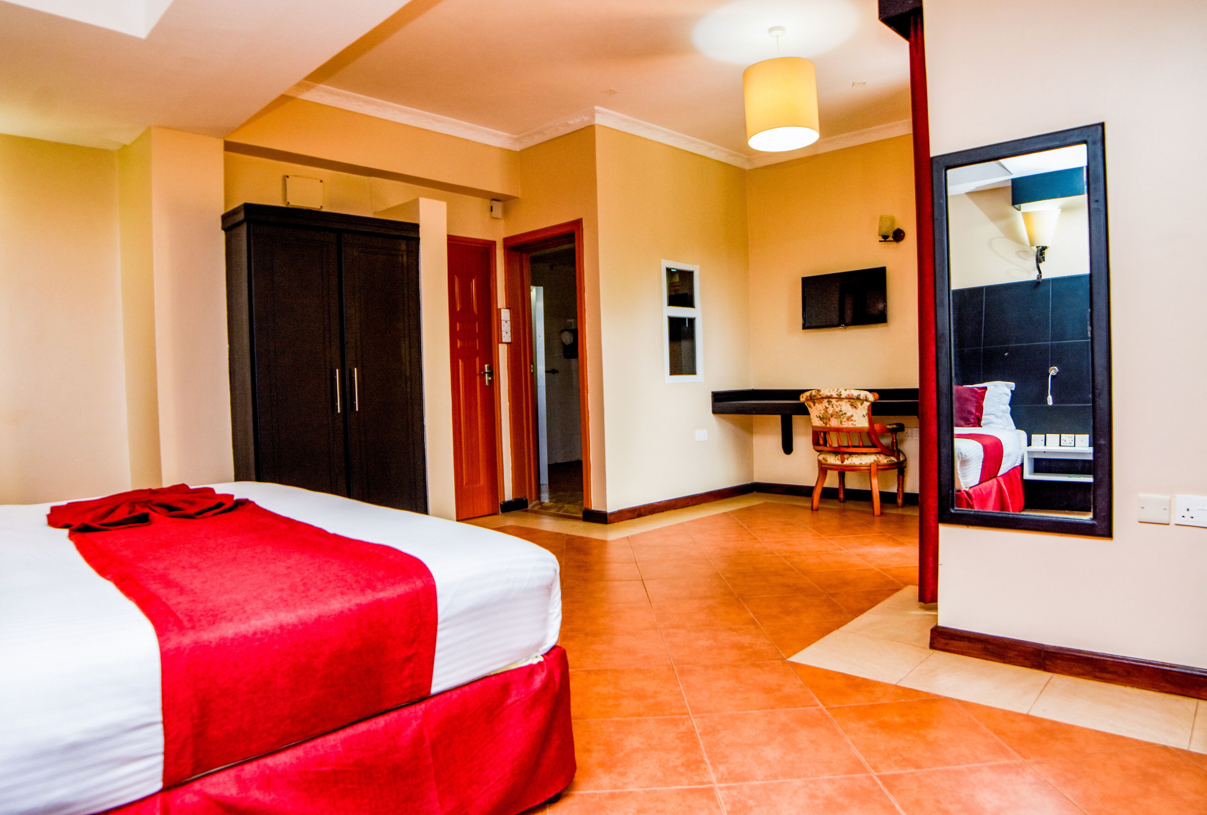 A hotel room with a bed, a desk, a chair, and a mirror.