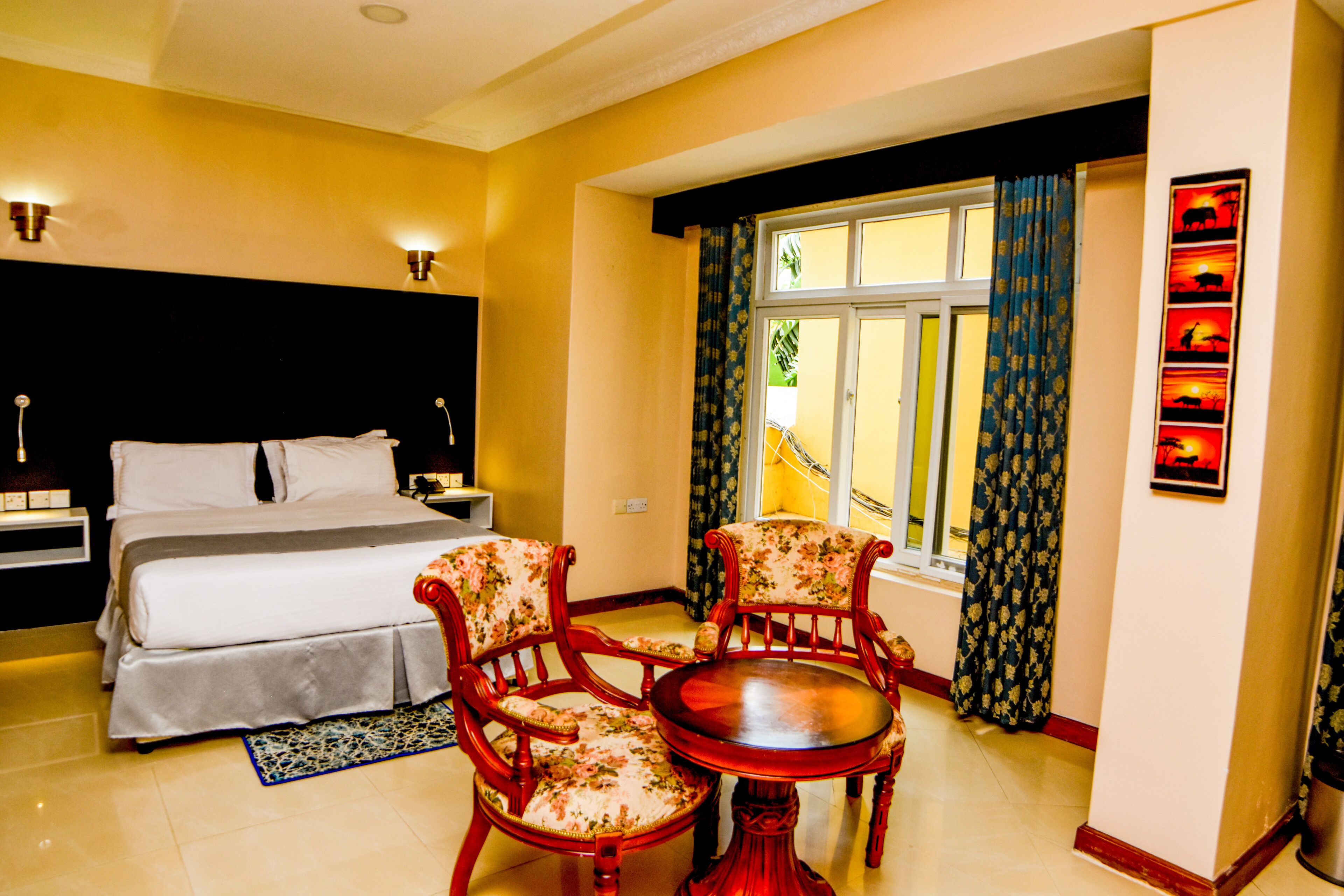 A hotel room with a bed, two chairs, a table, and a window with curtains.