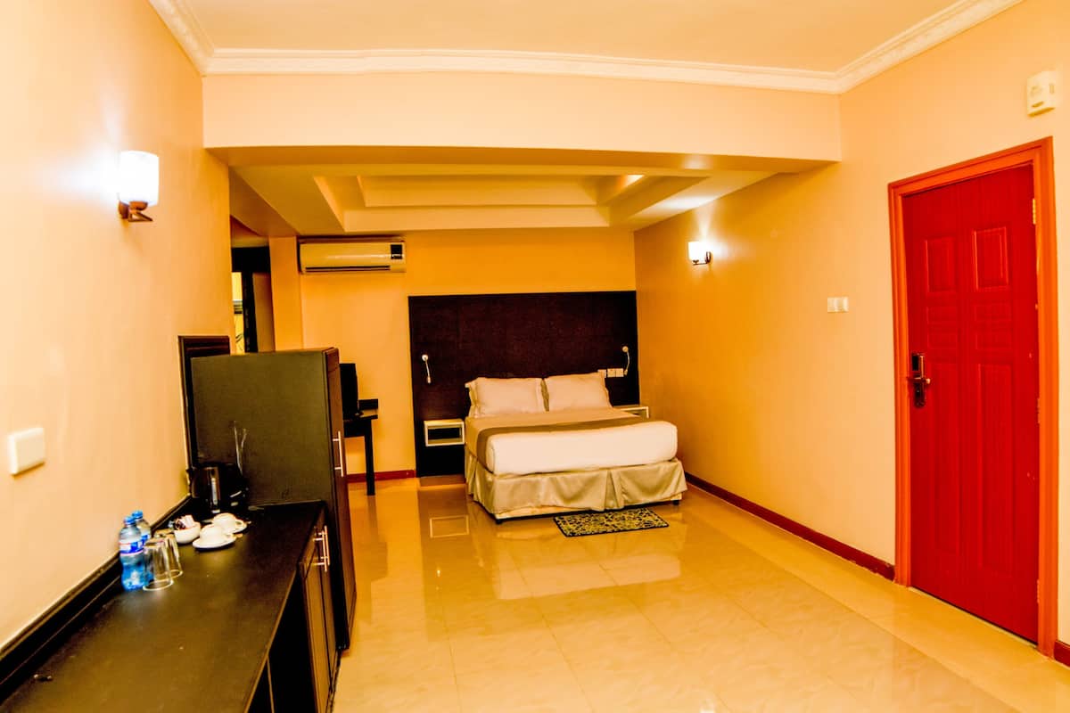A hotel room with a bed, bedside table, lamp, and a red door.