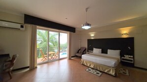 A hotel room with a large bed, a ceiling fan, a sliding glass door to a balcony, and a small table with chairs. - ISAMILO GRAND HOTEL (Mwanza)