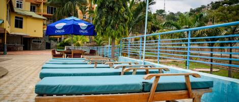 A pool area with wooden loungers and a blue umbrella.