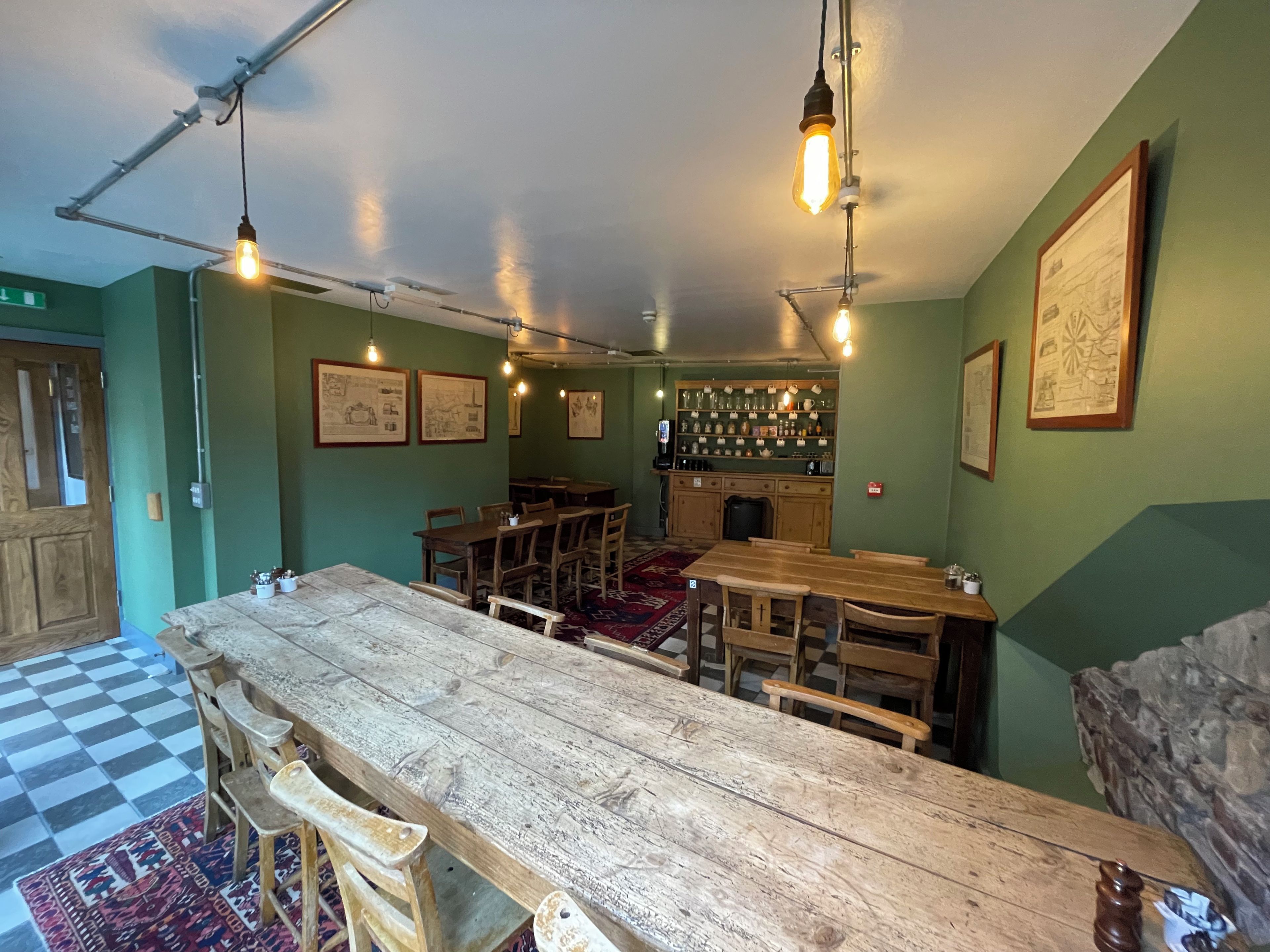 A bar area with wooden tables and chairs, hanging light fixtures, and framed artwork on the walls.