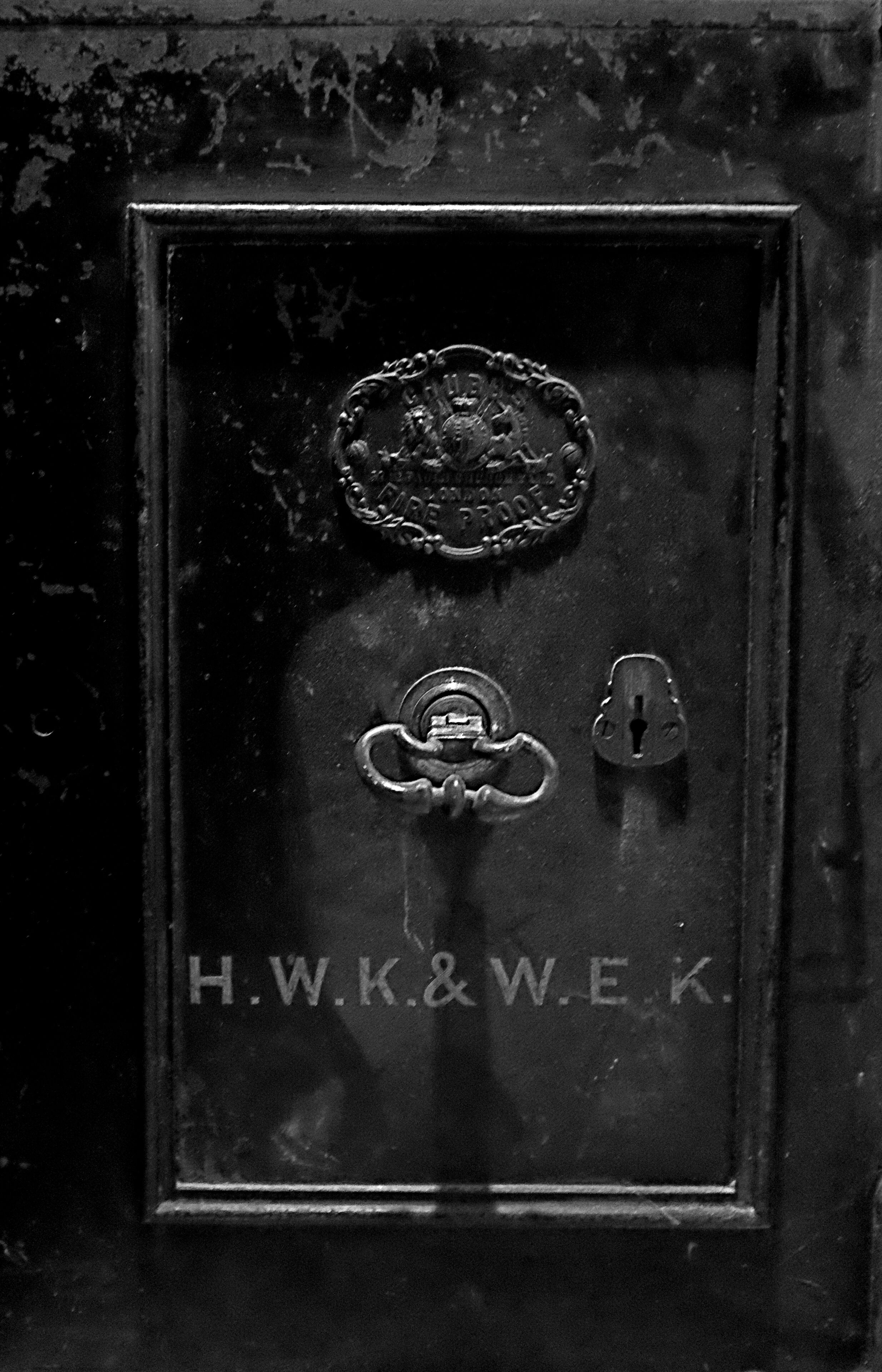 A black metal door with a brass lock and a keyhole. The door has a plaque with the inscription "H.W.K.&W.E.K."