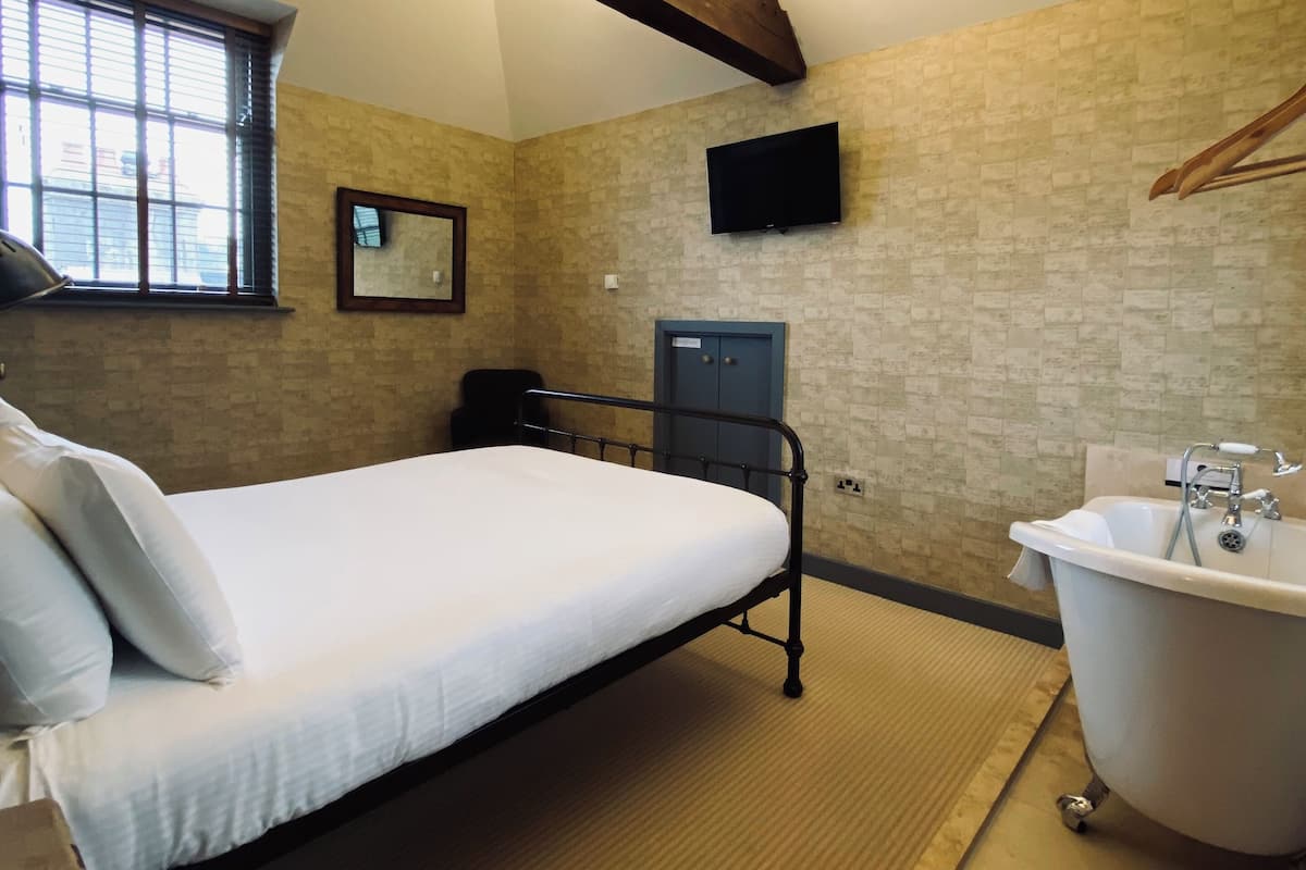 A bedroom with a bed, a wooden ceiling, a window, a TV, a door, and a bathtub.