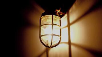 Un farol colgante con una cubierta de vidrio y estructura de metal, proyectando luz sobre una pared.