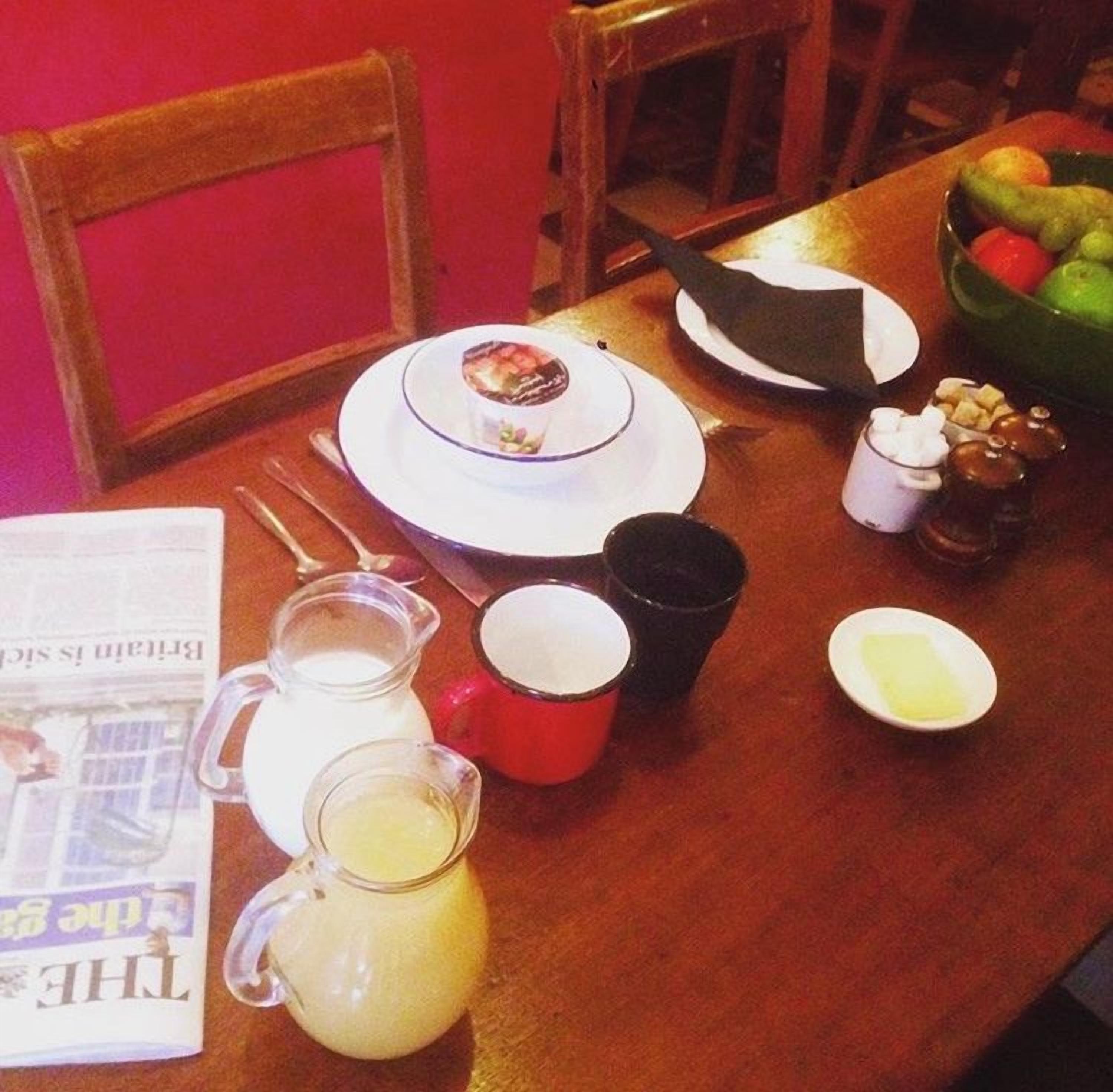 Una mesa de comedor con platos, tazas, una jarras y un cuenco de fruta.