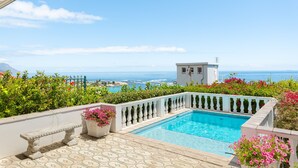 Un espace piscine avec vue sur la mer, un bâtiment blanc et des plantes en pot.