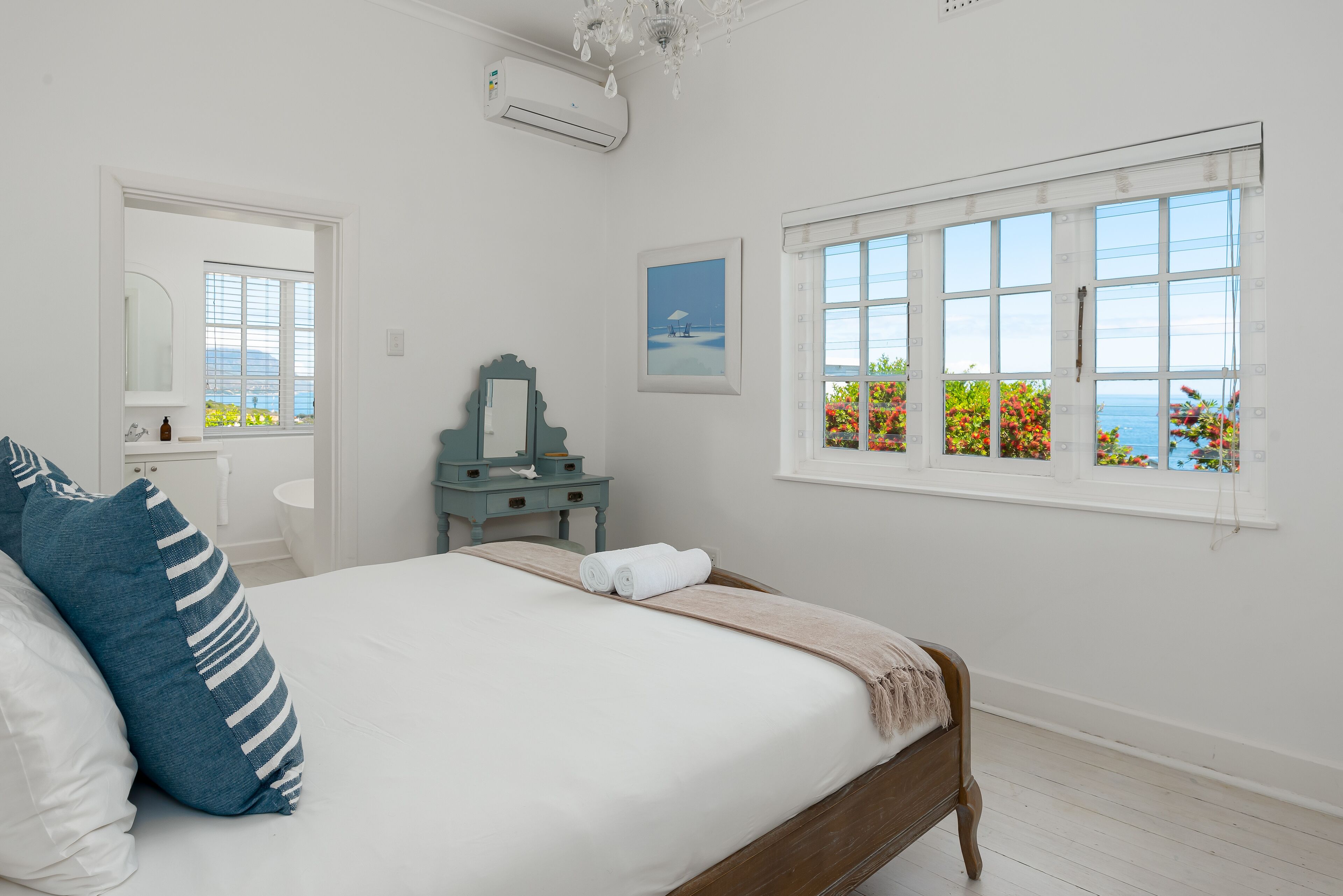 A bedroom with a large bed, a dresser, a mirror, and a window with a view.