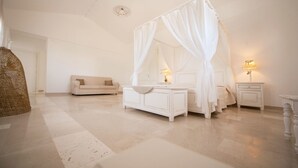 A bedroom with a four-poster bed, a bedside table with a lamp, a nightstand, a sofa, and a wicker chair. - Antica Masseria Ficazzana (Salve)