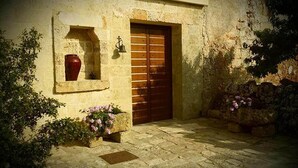 A stone building with a wooden door, a red vase in a window, and potted plants. - Antica Masseria Ficazzana (Salve)