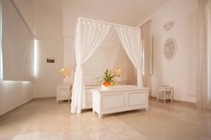 A bedroom with a four-poster bed, a bedside table with a lamp, a small bedside table, and a mirror on the wall. - Antica Masseria Ficazzana (Salve)
