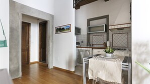A modern kitchen with a microwave, stove, and a hanging plant. There is a dining table with a white tablecloth and a chair.