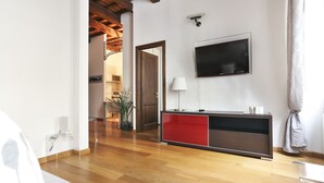 A modern living room with a wooden floor, a red and black entertainment unit, a mounted TV, and a door leading to another room.