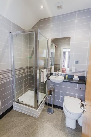 Een moderne badkamer met een douche met glazen wand, een wit toilet en een wastafel met spiegel.