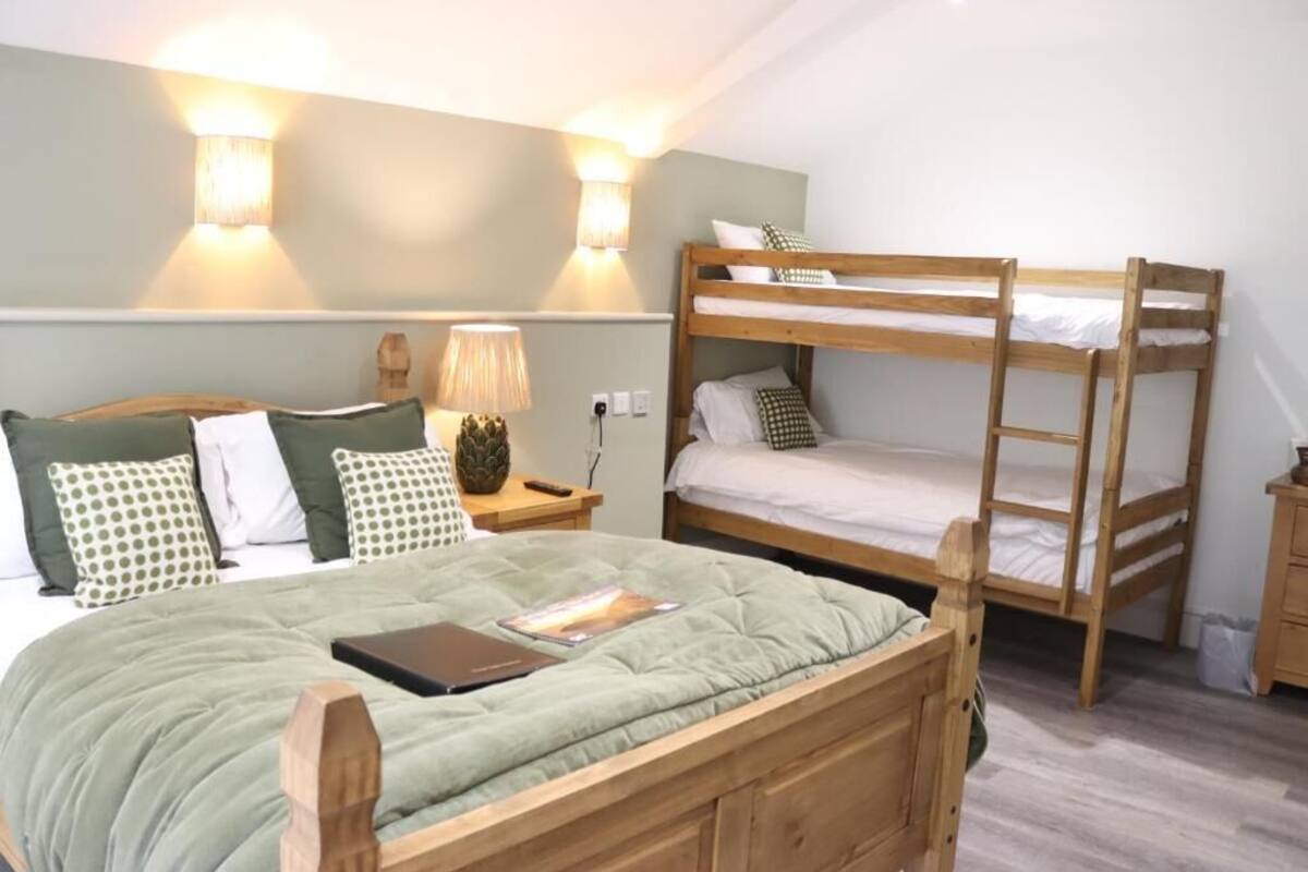 Un dormitorio con una cama litera, una cama individual, una mesita de noche con lámpara y una lámpara de pared.
