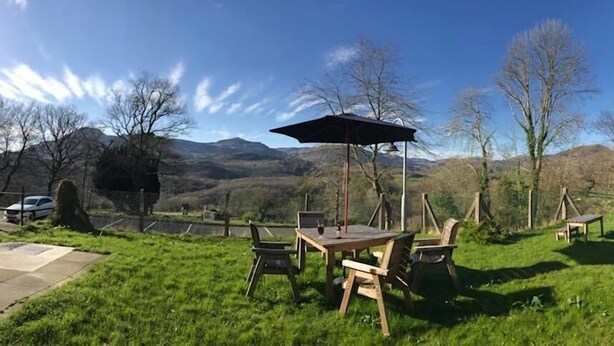 Ein Außenbereich mit Tisch und Stühlen, einem Holzzaun und Blick auf Hügel im Hintergrund.